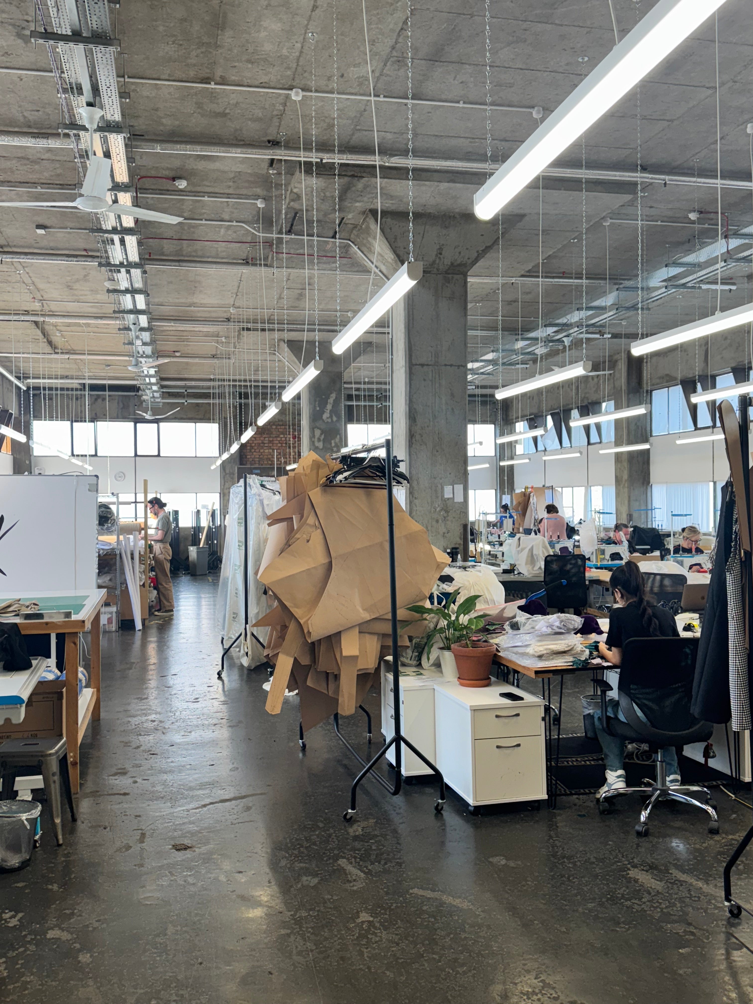 A fashion manufacturing studio in London for British modest dress brand, Kimesca. There a sewing desks, cutting tables and large pattern pieces hanging on rails.